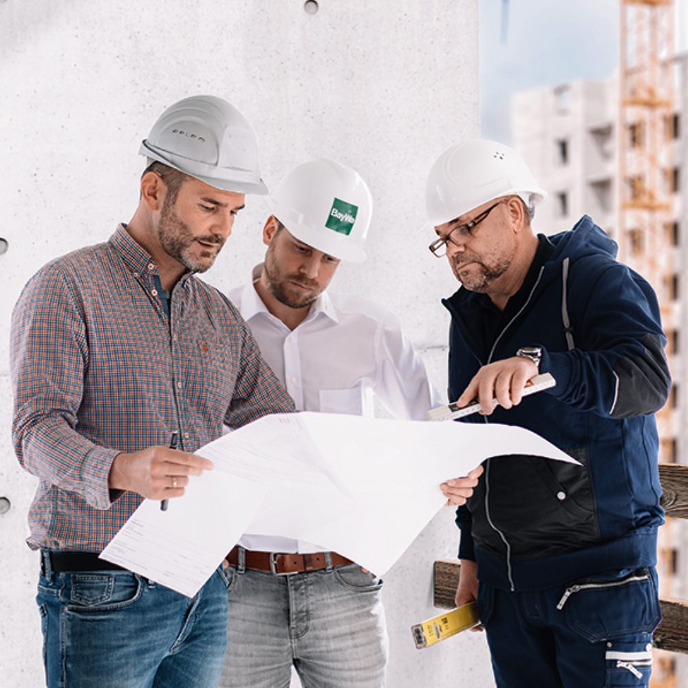 Drei Männer mit Helmen schauen auf einen Bauplan