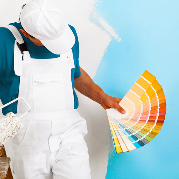 Ein Maler vor einer halb gestrichenen Wand mit einer Farbpalette in der Hand